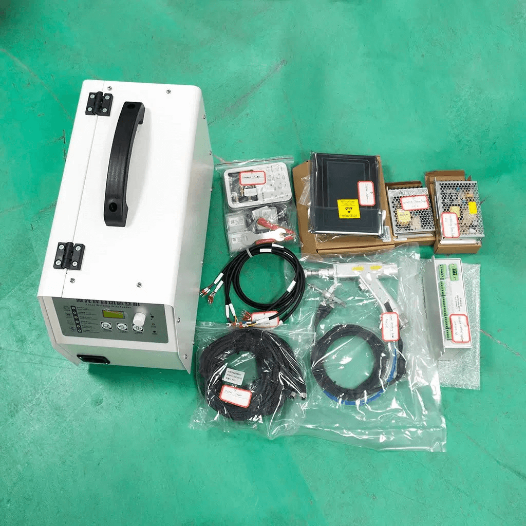 Laser welding system components and accessories on a green floor, including cables, control units, and power supplies.